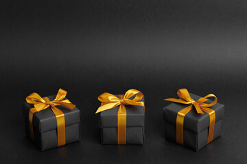 Black gift box with golden ribbon bow on black background