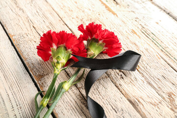 Beautiful carnation flowers with black funeral ribbon on white wooden background