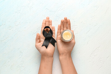 Woman holding black funeral ribbon and burning candle on light blue background