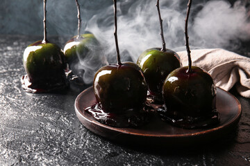 Plate with tasty caramel apples for Halloween on black background