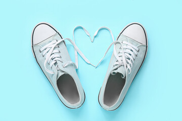 Stylish blue sneakers and heart made of laces on color background