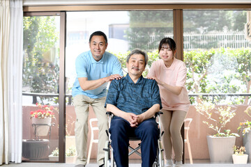 車椅子に乗る白髪のアジア人の高齢者とアジア人の男女の介護士
