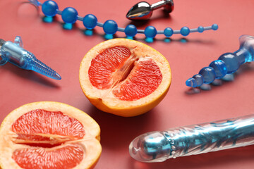 Different sex toys and tasty grapefruit on red background, closeup