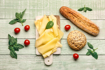 Board with tasty cheese slices, basil leaves, tomatoes and bread on color wooden background