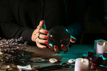 Witch with crystal ball at dark wooden table, closeup