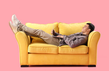 Young man using laptop on sofa against pink background