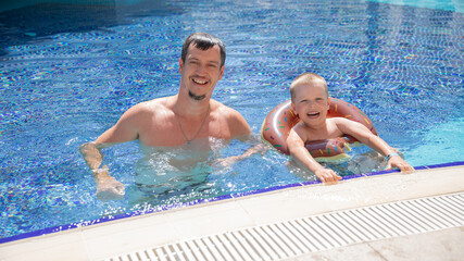 Little boy and his father bathing in swimming pool with lifebuoy donut, smiling and happy
