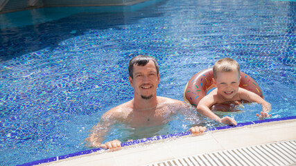 Little boy and his father bathing in swimming pool with lifebuoy donut, smiling and happy