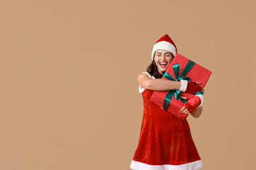 Happy young woman in Santa Claus costume with Christmas gift box on brown background