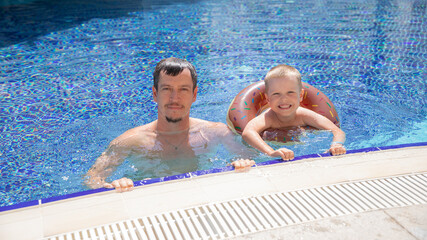 Little boy and his father bathing in swimming pool with lifebuoy donut, smiling and happy