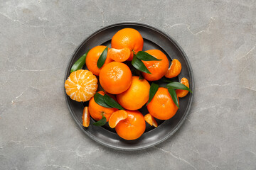 Plate with sweet mandarins and leaves on grey background