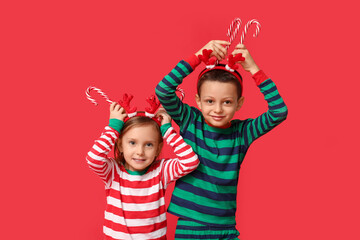 Funny little children in pajamas with candy canes on red background