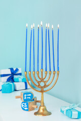 Menorah with burning candles and dreidels on white cabinet near blue wall. Hanukkah celebration
