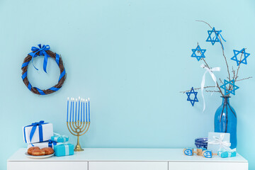 White cabinet with menorah, dreidels, sufganiyots and gift boxes near blue wall. Hanukkah...