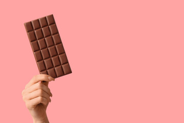 Female hand with chocolate bar on pink background