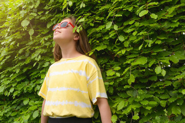 Enjoy summer. A teenage girl in red sunglasses and a yellow t-shirt. Against a background of green...