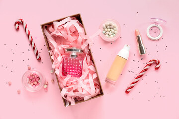 Gift box with bottle of perfume, cosmetic products and Christmas decorations on pink background