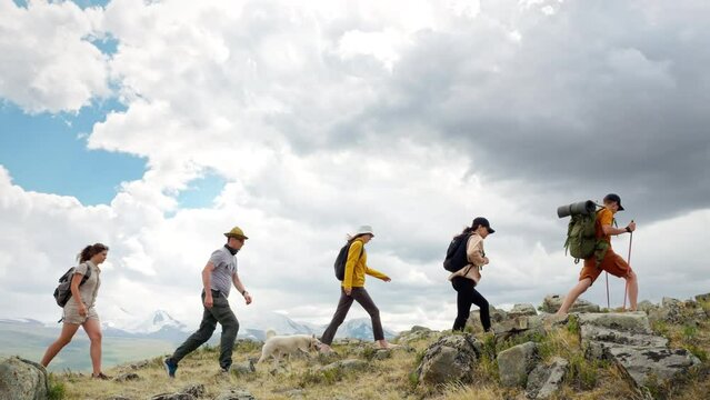 Group of five young hikers go path uphill to mountain top along wild rocky area at scenic side view. Active travel recreation, tourist trekking and motivation to sport trail