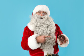 Santa Claus pointing at tasty donut on blue background