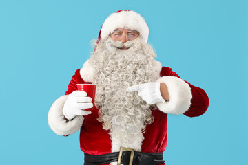 Santa Claus pointing at cup of tea on blue background