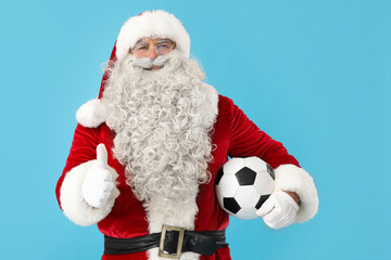Santa Claus with soccer ball showing thumb-up on blue background