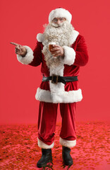 Santa Claus with glass of beer pointing at something on red background