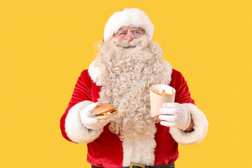 Santa Claus with tasty burger and french fries on yellow background