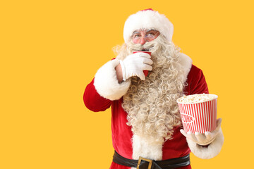 Santa Claus with cup of cola and tasty popcorn on yellow background