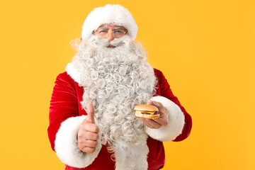 Santa Claus with tasty burger showing thumb-up on yellow background