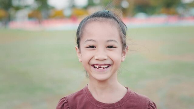 Lush greenery of a playground, close up Asian adorable 7-year-face with innocence and positivity. Her radiant smile and expressive face exude happiness, the laughter of children playing freely.