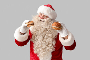 Santa Claus with tasty burgers on white background
