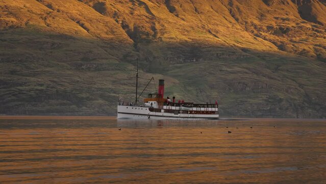 Old steamboat traveling on calm alpine lake with mountain backdrop