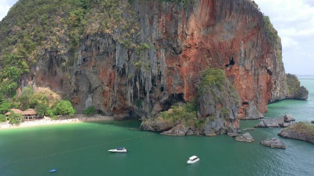 Panning drone shot of Phra Nang Beach's impressive limestone cliff with jagged rocks and a nice deep reddish hue to the cliffs. Home of Princess bay in southern Thailand region.