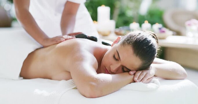 Woman, massage and hot stones to relax, back and spa for physical therapy, treatment and asleep. Body care, masseuse and wellness with candles, peaceful and hands in luxury resort and tranquility