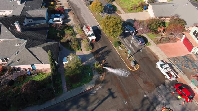 Working on a fire hydrant in Santa Cruz - water gushing on the suburban street - aerial tilt up reveal