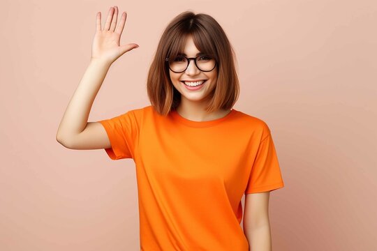 Full shot of slender young woman with fair amber straight chest length hair and bangs in an orange cut-off t-shirt and sunglasses, smiling and waving at the camera on a blank background