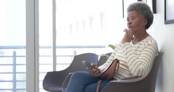 African american senior woman using smartphone in hospital waiting room, slow motion