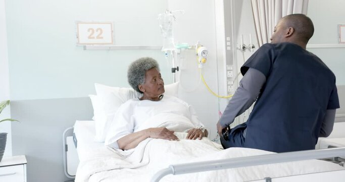 African american male doctor talking with female senior patient in hospital room, slow motion