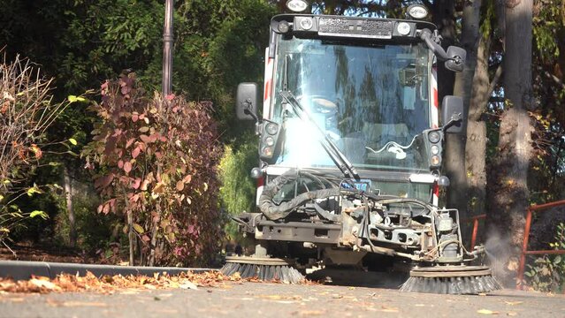 machine that cleans public sidewalks in a park. leaves picked up by a cleaning machine. 4k video.