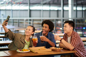 Cheerful diverse group of friends taking selfie in cafe when having lunch together