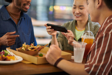 Young woman taking picture of street food when having lunch with friends