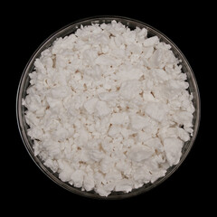 Cottage cheese in glass bowl isolated on black background. Top view of Pressed dairy solids
