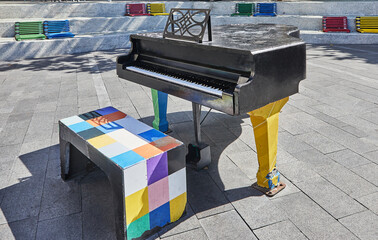 Black piano in the city square, colored benches around. Music concept