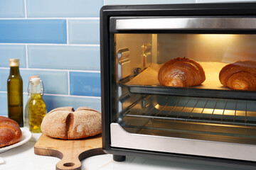 Modern mini electric oven with freshly baked croissants in kitchen
