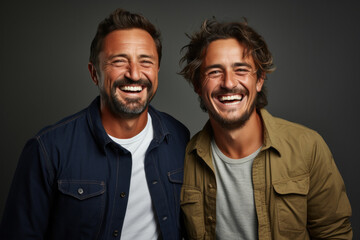 Young happy gay couple in casual clothes isolated on gray background - obrazy, fototapety, plakaty