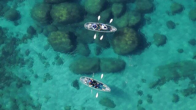Overhead drone shot of transparent blue water with large rocks on lake bed from above. Aerial view couple of tourists rowing in clear kayak in lake Tahoe exotic destination with turquoise calm water