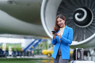 Business woman, traveler waiting for flight in airport, standing with luggage, using smartphone,...