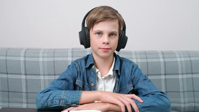 Distance learning online by video call, teen boy sitting at workplace in living room and uses a webcam to study in self-isolation at home, the boy in headphones.