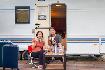 Senior asian couple joyful and relax sitting in front of caravan home on vacation. - obrazy, fototapety, plakaty