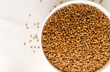 Organic dry buckwheat groats in a white bowl on a light background. Vegetarian and vegan food. Concept of healthy eating. Horizontal orientation. Top view. Copy space